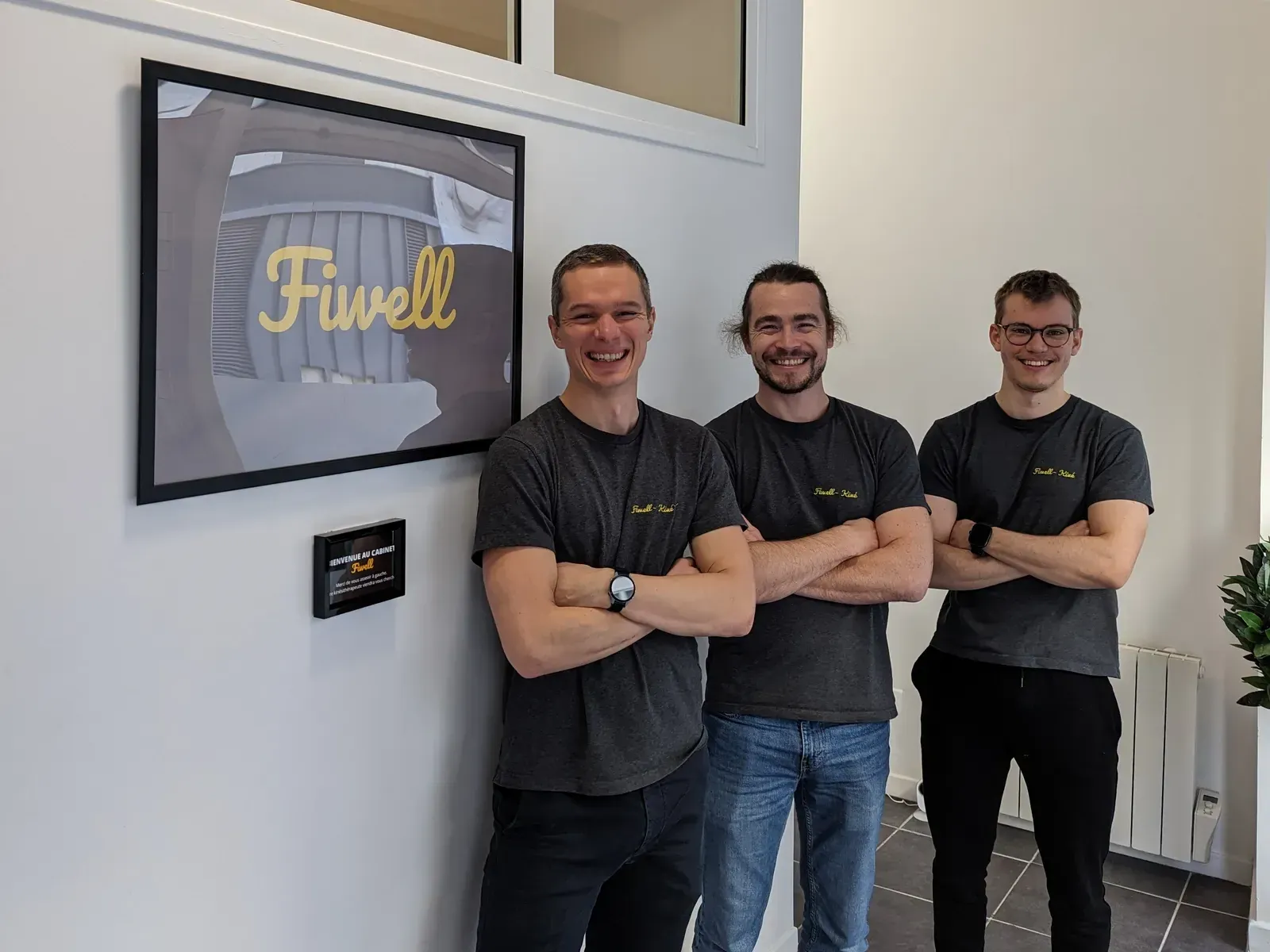 Trois kinésithérapeutes de l'équipe Fiwell, en tee-shirt Fiwell Kiné, à l'accueil du cabinet de Courbevoie